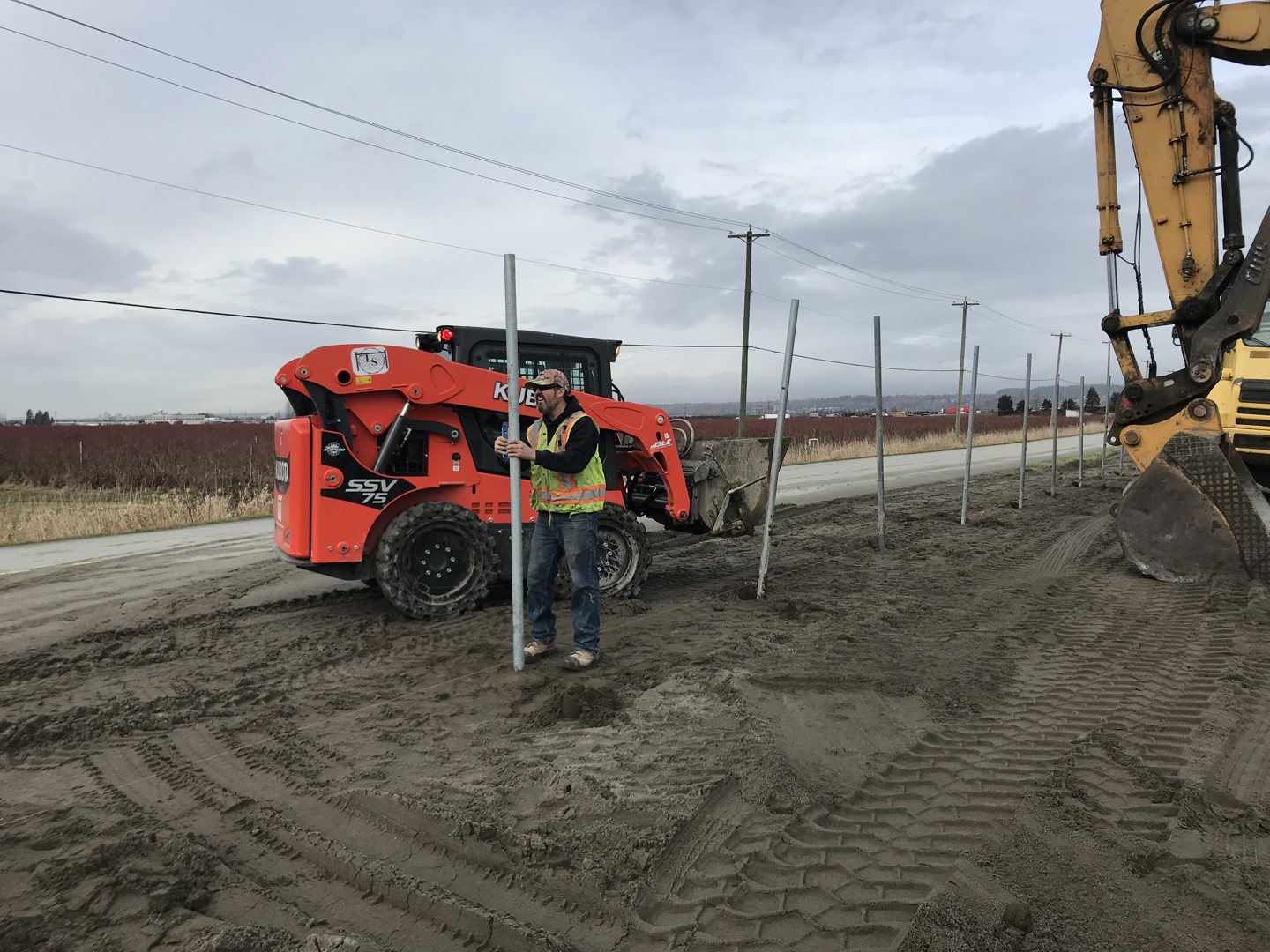 Loader and auger along a fence-post line.
