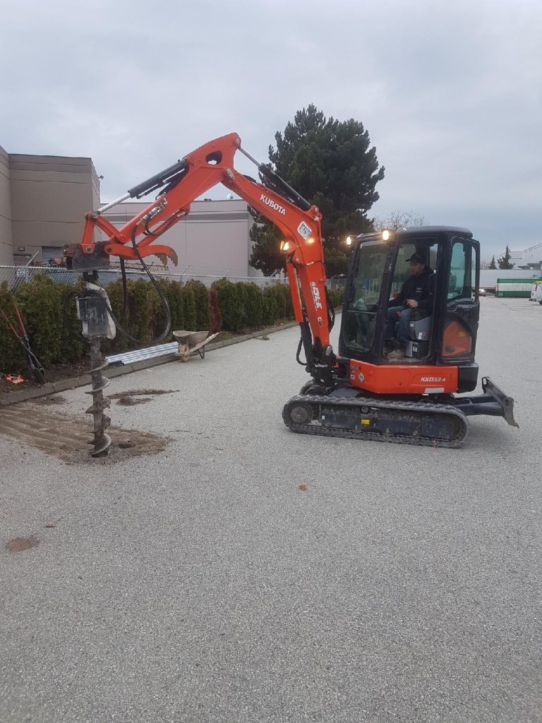 Compact excavator with an auger at a fence-work site.